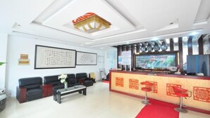 Un área de recepción con alfombra roja, sofás de cuero negro, un mostrador de recepción y una pantalla de televisión.