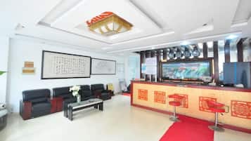 A hotel lobby with a reception desk, seating area, and a red carpet.