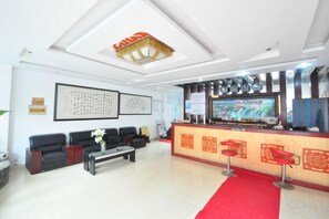 Un hall d’hôtel comprenant un comptoir d’accueil, un espace salon et un tapis rouge.