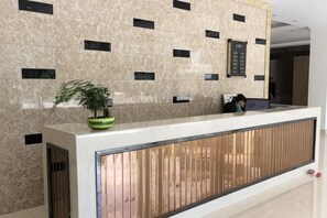 A reception desk with a potted plant, a wooden panel, and a wall-mounted elevator control panel. - Green Island Hotel (Daxin)