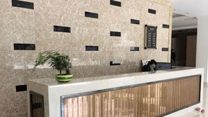 A reception desk with a potted plant, a digital display, and a wooden panel design. - Green Island Hotel (Daxin)