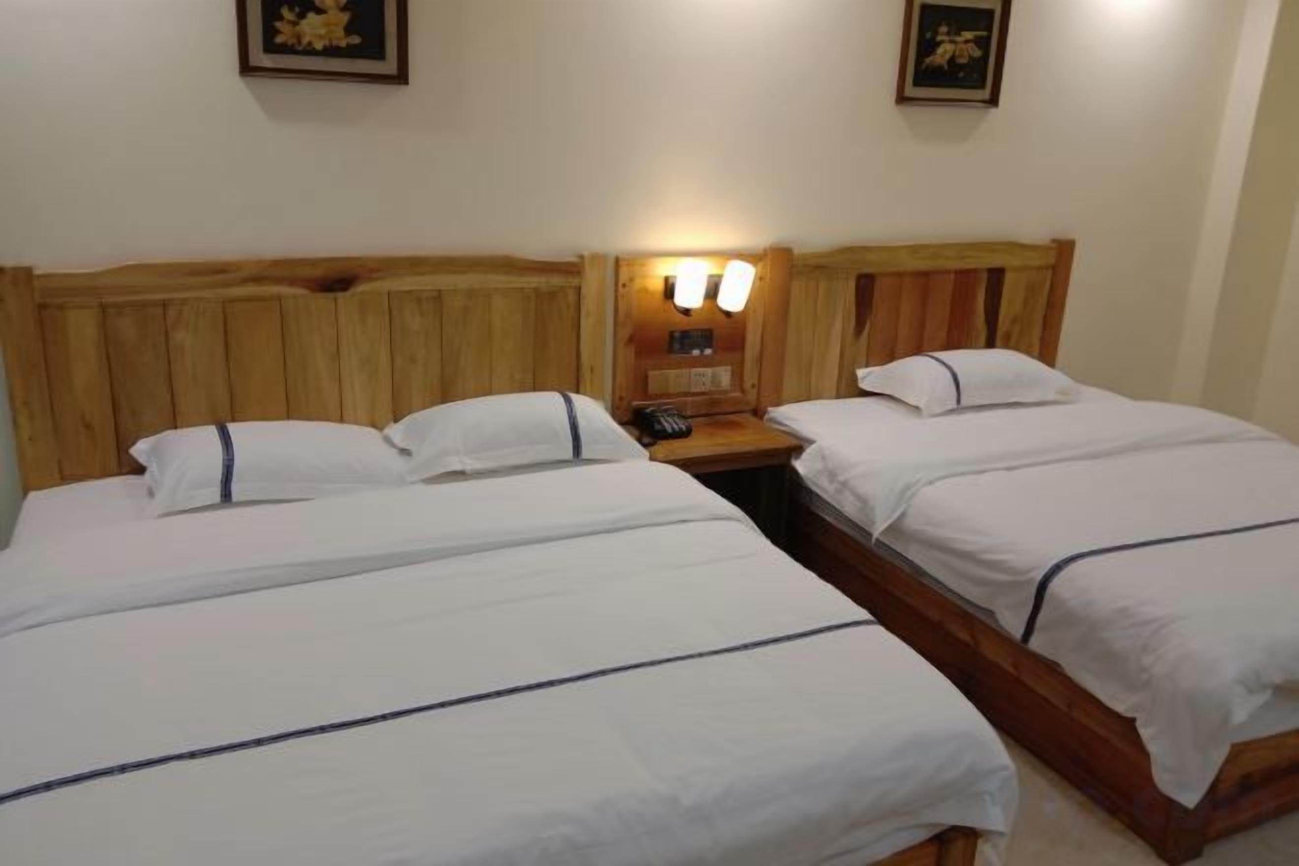 A double room with two beds, wooden headboards, bedside lamps, and a nightstand with a phone.