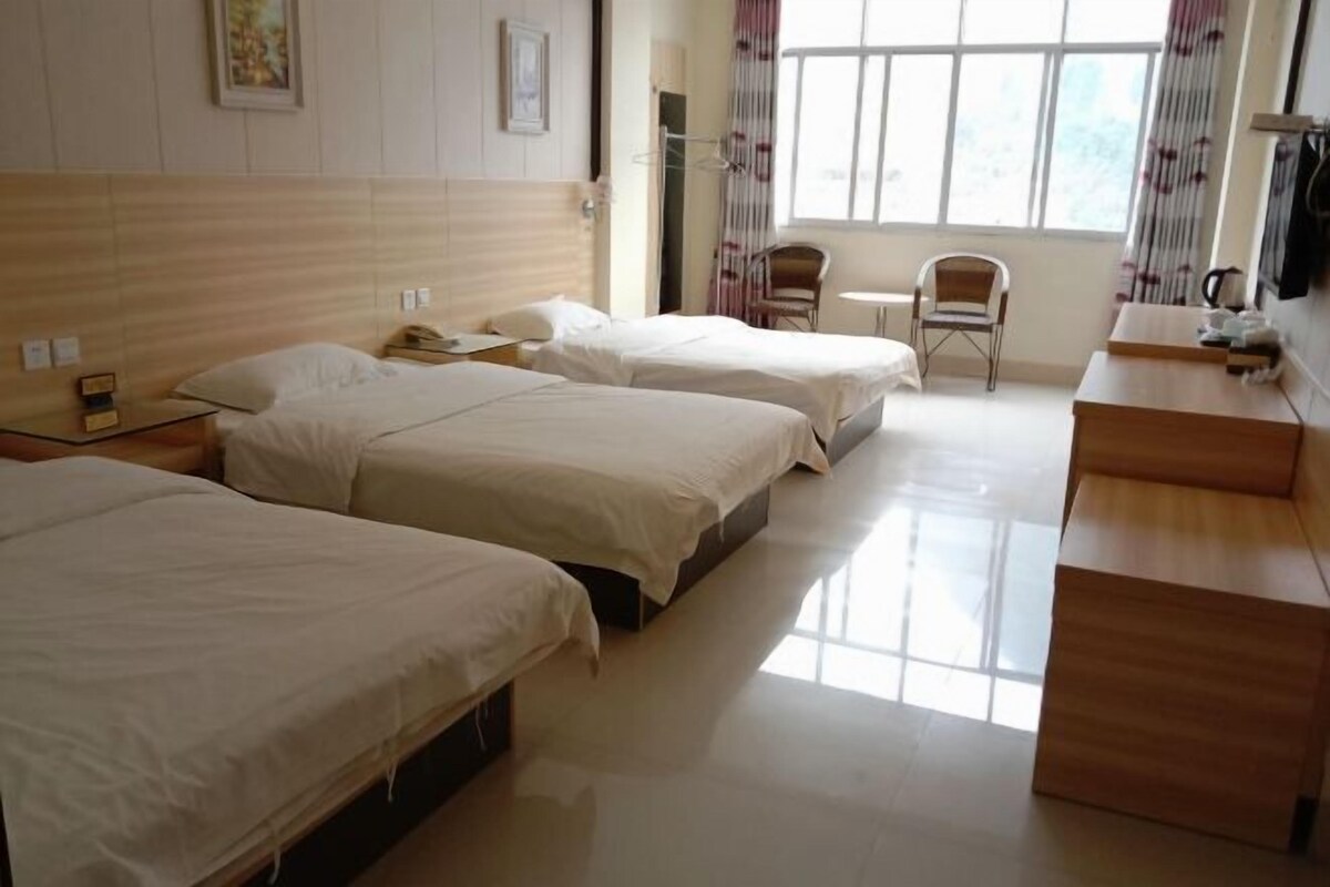 A hotel room with three beds, a small table, a chair, and a window with curtains.