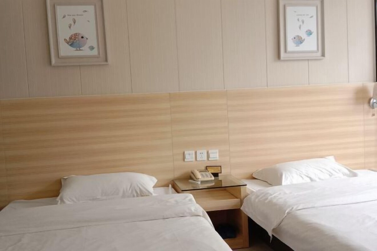 A hotel room with two beds, a wooden headboard, a bedside table with a phone, and framed artwork on the wall.