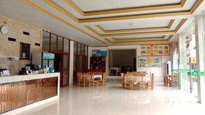 A hotel lobby with a reception desk, wooden chairs, a clock, and a menu board. - Green Island Hotel (Daxin)