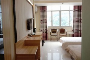 A hotel room with a wooden desk, two chairs, a small table, and two beds. - Green Island Hotel (Daxin)