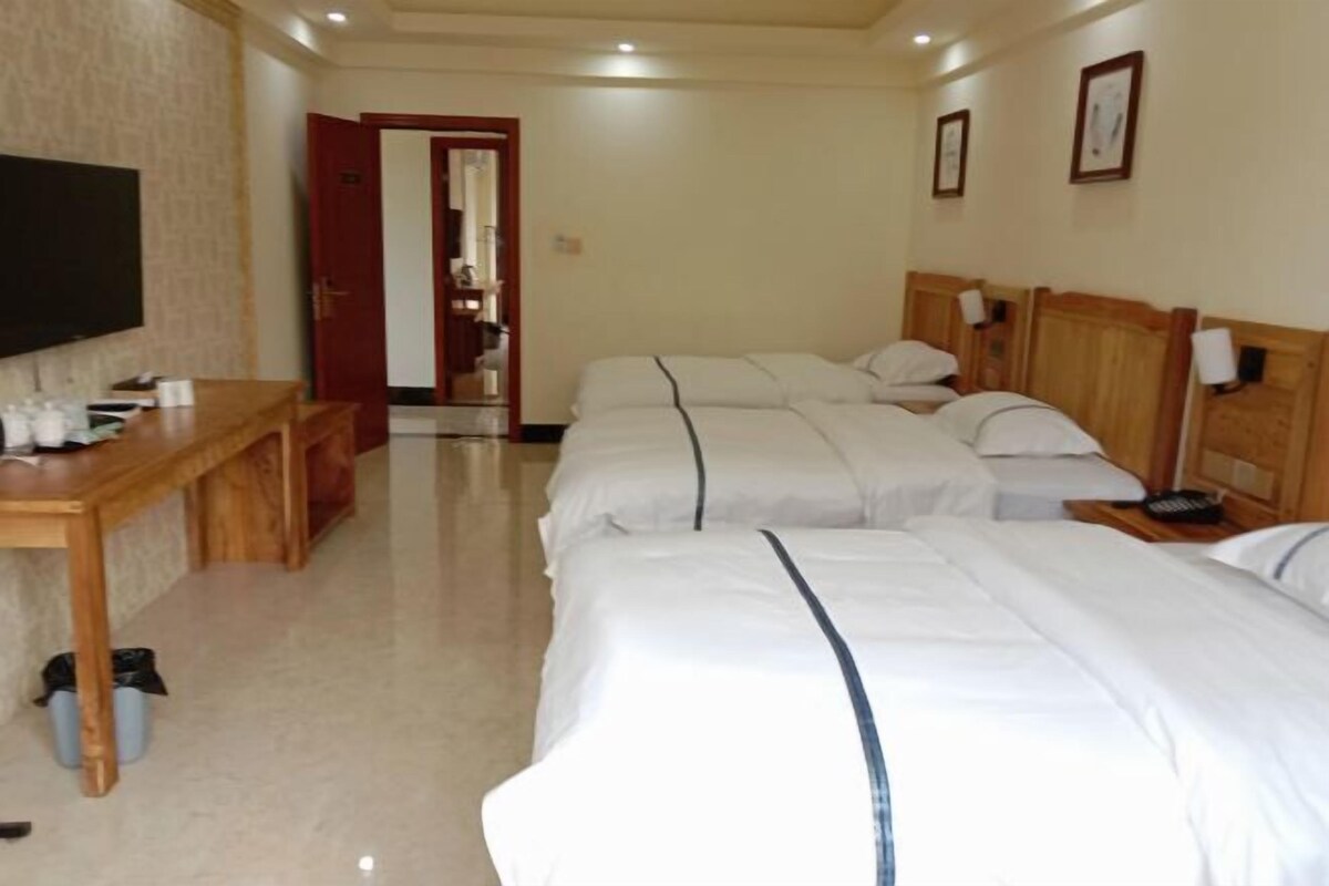A hotel room with three beds, a wooden desk, a television, and a door leading to a bathroom.