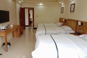 A hotel room with three beds, a wooden desk, a television, and a door leading to a bathroom. - Green Island Hotel (Daxin)