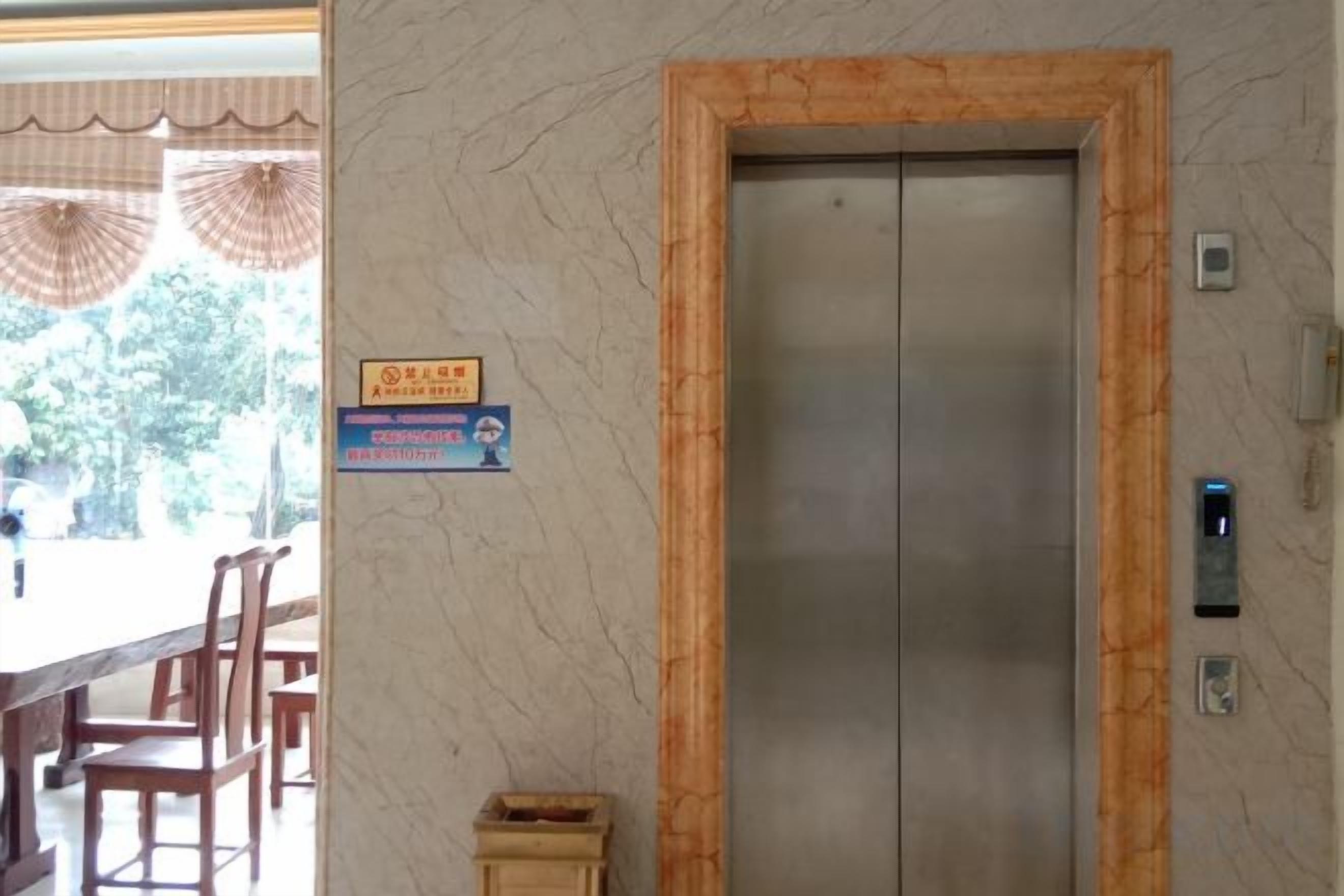 Un ascensor con pared de mármol y estructura de madera, un cartel con texto y una mesa con sillas.