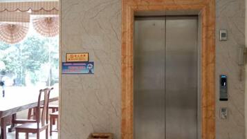 Un ascensor con pared de mármol y estructura de madera, un cartel con texto y una mesa con sillas.