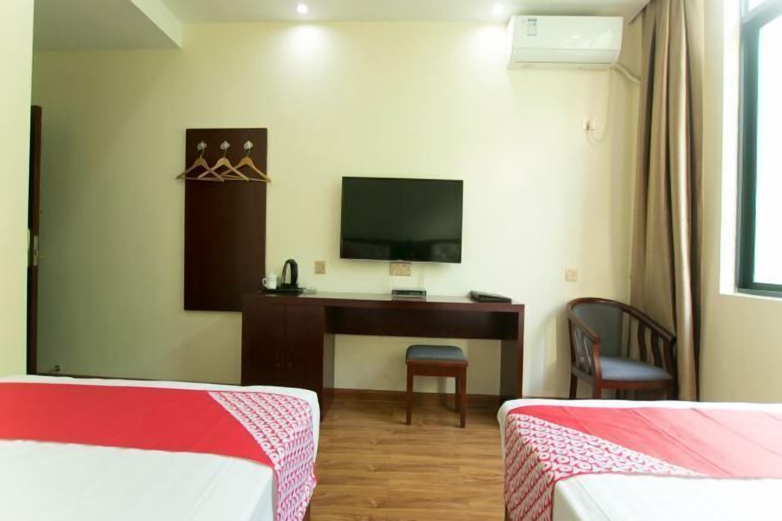 A hotel room with two beds, a desk, a chair, a TV, and a coat rack.