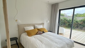 Un dormitorio moderno con una cama grande, un banco y vistas a zonas verdes a través de un gran ventanal corredizo.