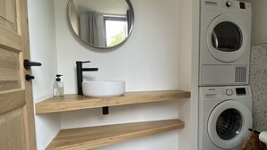 Un baño moderno con tocador de madera, espejo redondo, lavamanos blanco y lavadora y secadora apiladas.