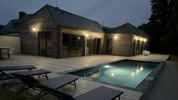 Una casa moderna con piscina, terraza de madera y sillones de descanso.