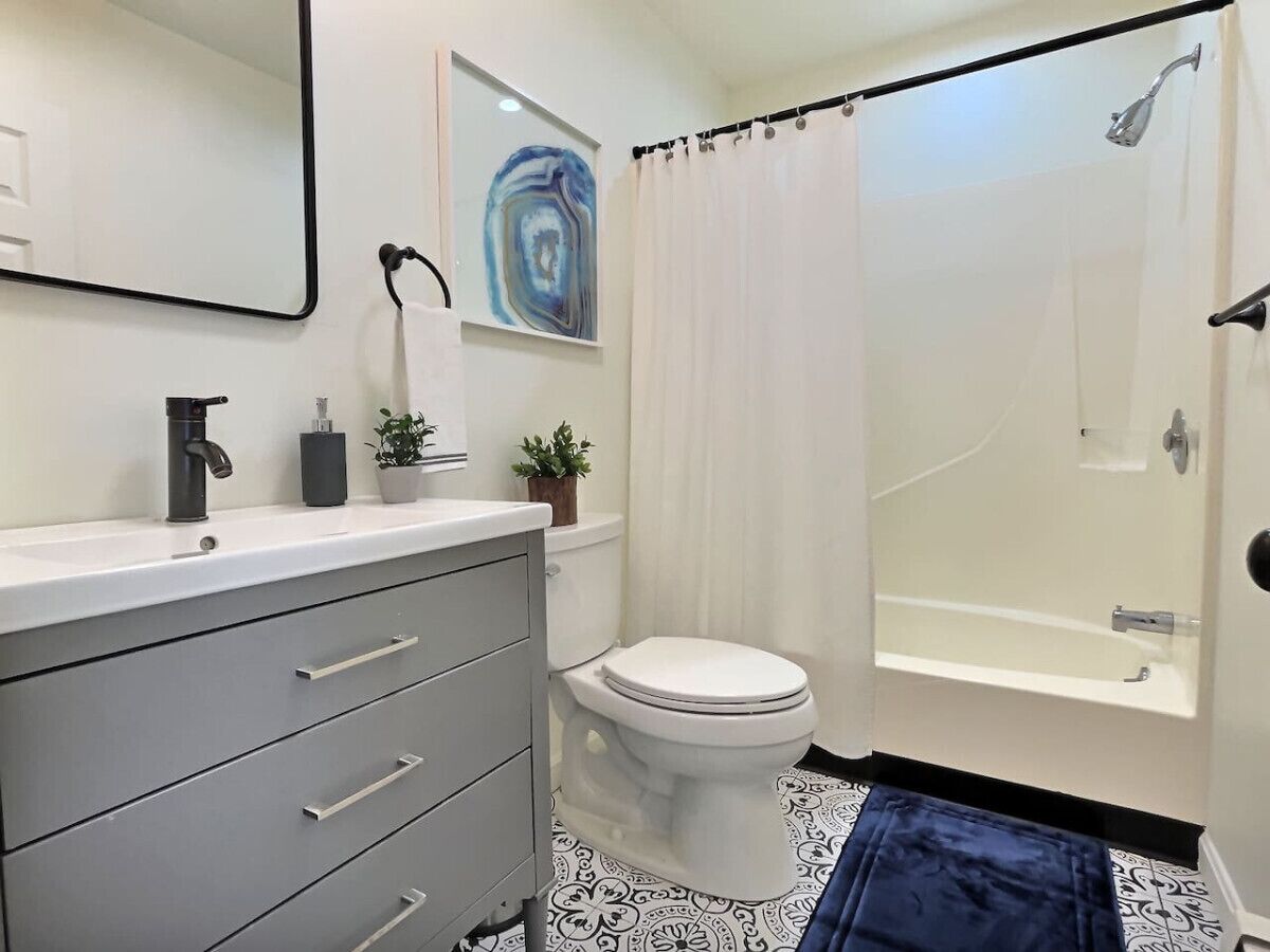 A bathroom with a toilet, a sink, a mirror, a shower, and a curtain.