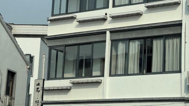 A multi-story building with large windows and a sign with Chinese characters. - Shanerqi Homestay in Xinchang (Xinchang)
