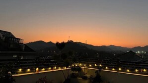 A hotel with a rooftop terrace, a view of the mountains, and a sunset in the background. - Shanerqi Homestay in Xinchang (Xinchang)