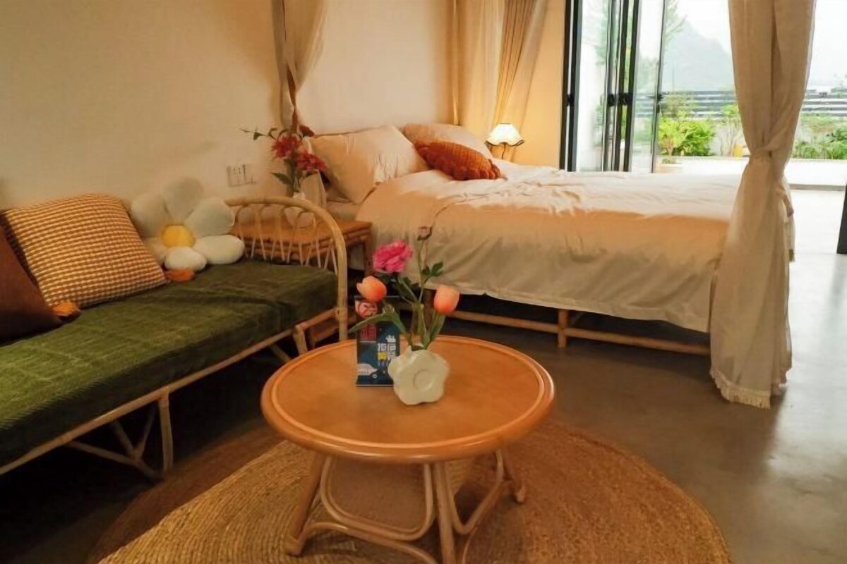 Ein Schlafzimmer mit einem Bett, einem grünen Sofa, einem runden Holztisch und einem Fenster mit Vorhängen.