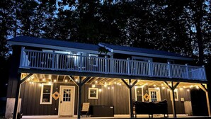 A two-story wooden cabin with a balcony, a porch with string lights, and a front door.