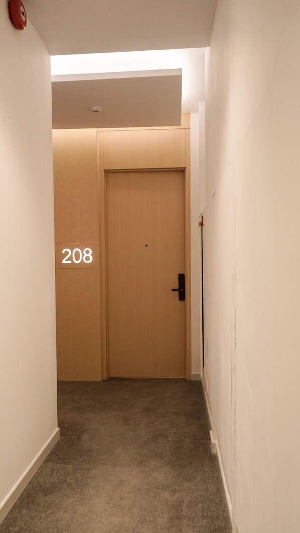 Un couloir doté d’un sol recouvert de moquette, une porte en bois portant le numéro 208 et un détecteur d’incendie sur le mur gauche.