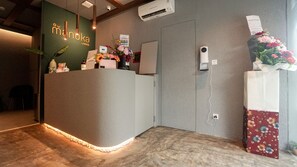 Ein Empfangsbereich mit grüner Wand, einer Rezeption, einer Blumenkomposition und einer Klimaanlage.