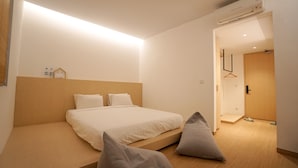 A minimalist bedroom with a large bed, a wooden headboard, and a small bedside table with a lamp. - Manuka By Havis Hotel at Penuin (Batam)