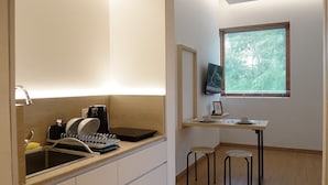 A modern kitchen with a built-in stove, sink, and a dining area with a table and two chairs. - Manuka By Havis Hotel at Penuin (Batam)
