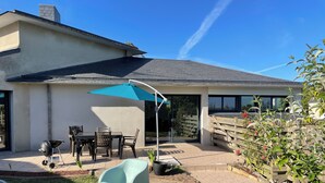 A patio area with a table, chairs, a grill, and a blue umbrella.