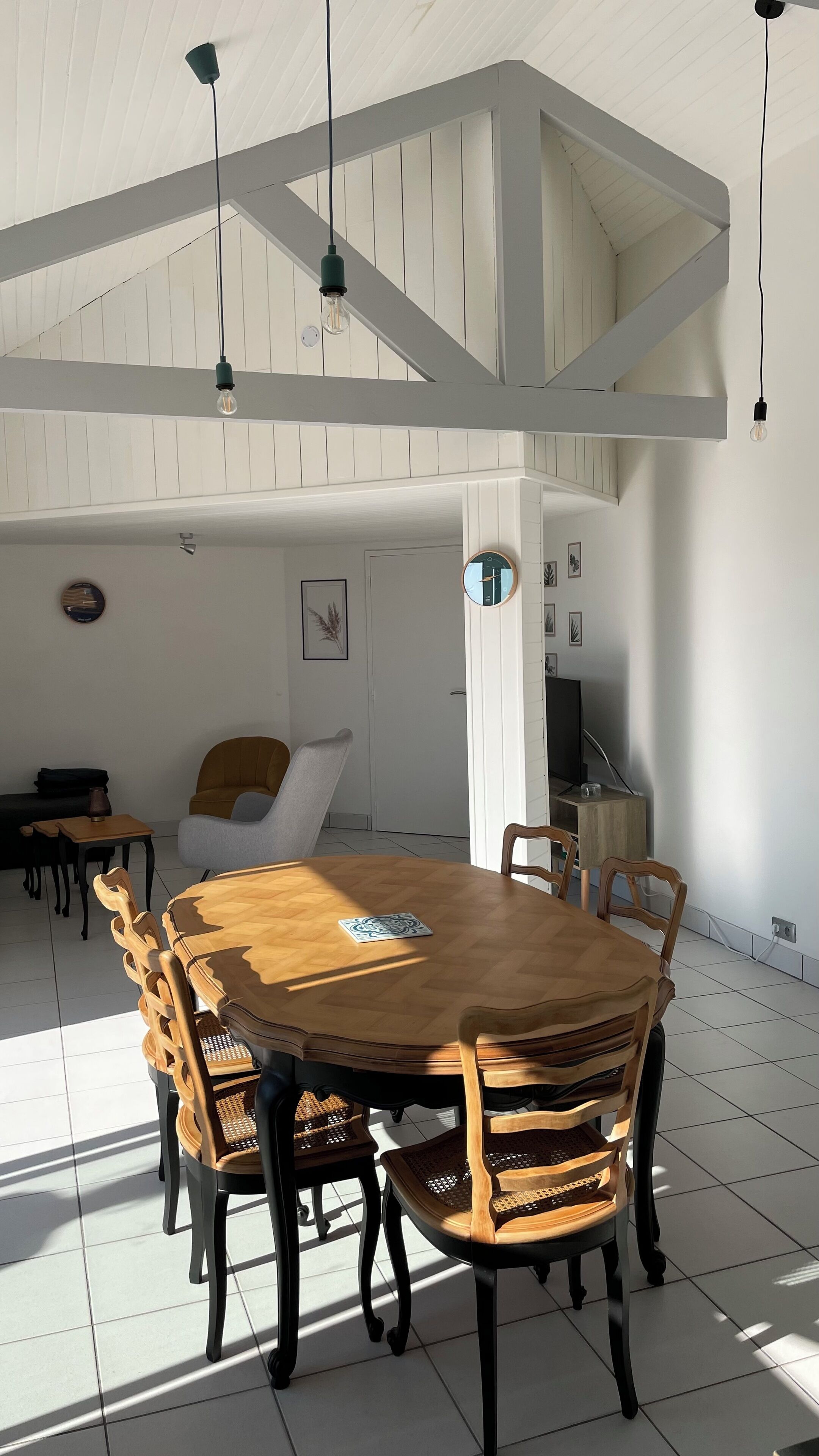 A spacious dining area with a wooden table and chairs, white walls, and a high ceiling with exposed beams.