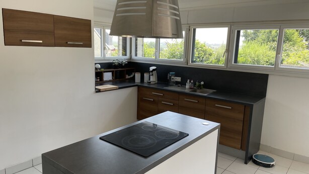 A modern kitchen with a built-in stove, dark countertops, wooden cabinets, a window with a view of greenery, and a ceiling light fixture.