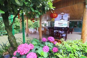 An outdoor dining area with tables and chairs, surrounded by potted plants and a tree. - Mingxiuya Leisure Villa (Emeishan City)