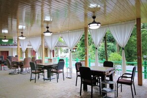 An indoor dining area with tables and chairs, a wooden ceiling, and large windows with white curtains. - Mingxiuya Leisure Villa (Emeishan City)