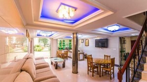 A spacious living area with a sofa, dining table, and chairs, a staircase, and a TV mounted on the wall. - Mingxiuya Leisure Villa (Emeishan City)