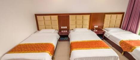 Ein Hotelzimmer mit vier Einzelbetten, jeweils mit weißer Bettdecke und orangefarbenem Zierstreifen. Das Zimmer verfügt über ein Holz-Kopfteil mit einer gepolsterten Struktur und einer Wand in neutralen Farben.