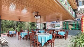 An outdoor dining area with round tables and chairs, covered by a wooden roof, and a signboard in the background.