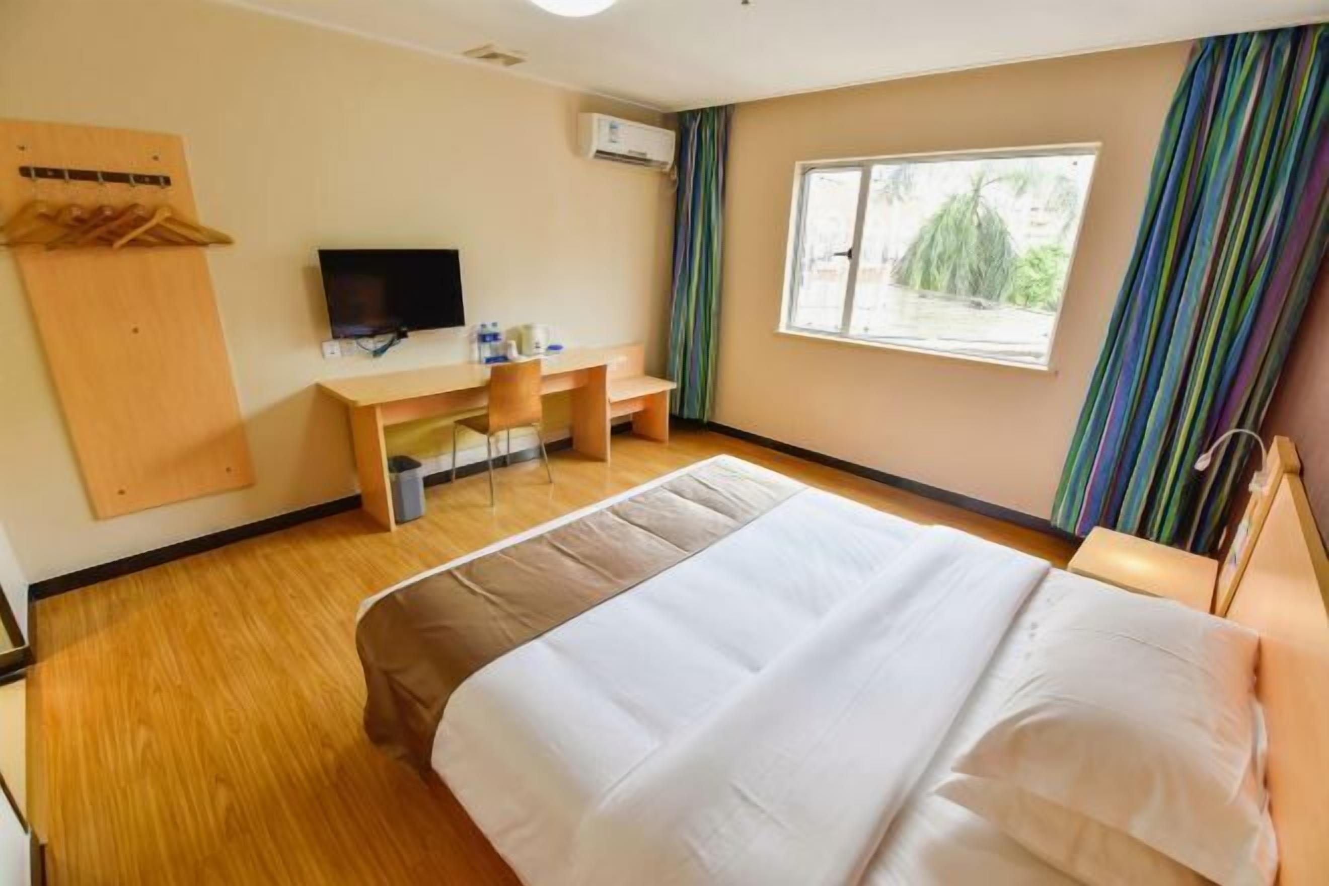 A hotel room with a bed, a desk with a chair, a television, and a window with curtains.