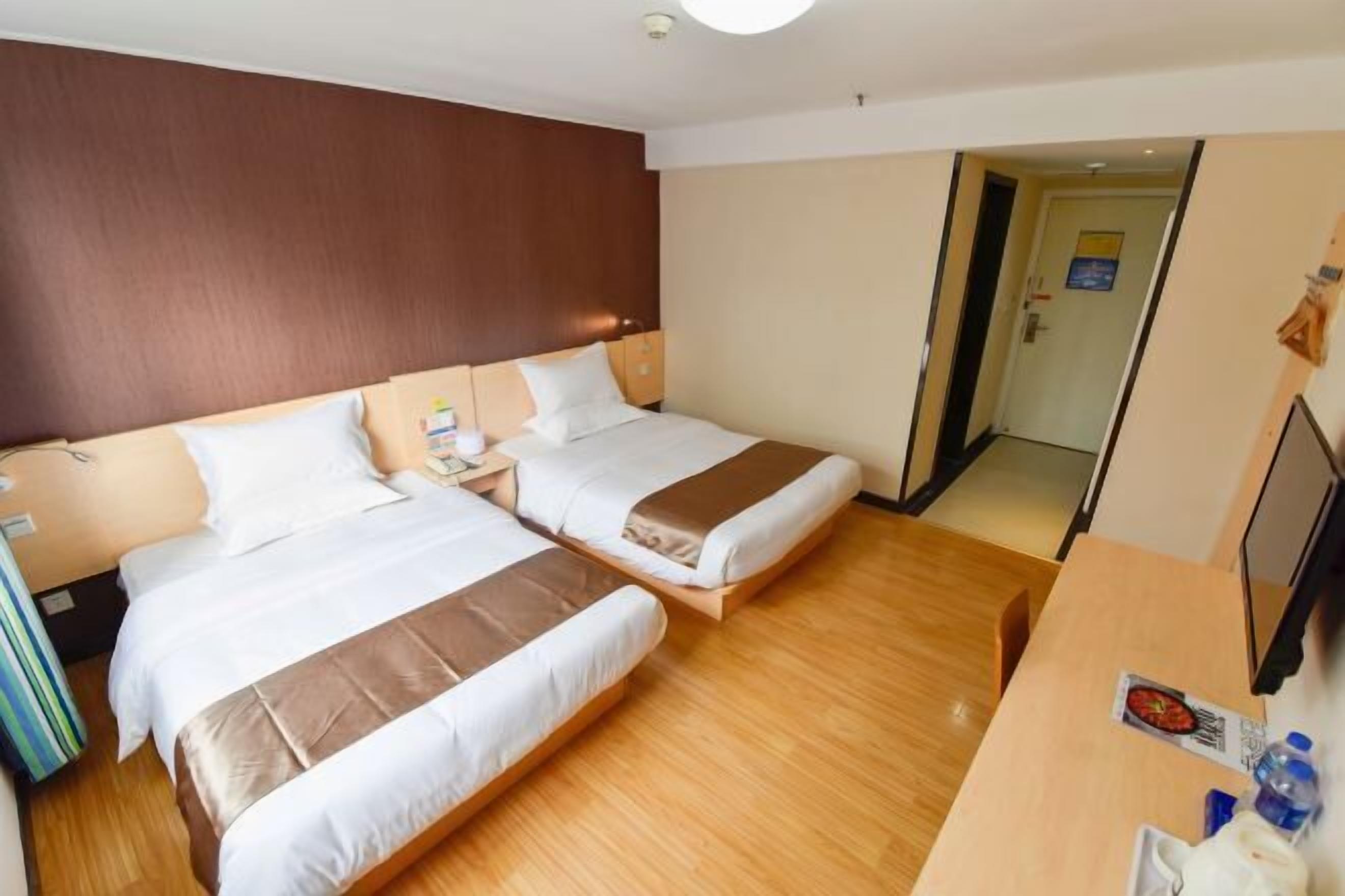 Ein Hotelzimmer mit zwei Betten, Holzboden, Schreibtisch mit Stuhl und Fernseher.