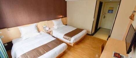 Ein Hotelzimmer mit zwei Betten, Holzboden, Schreibtisch mit Stuhl und Fernseher.