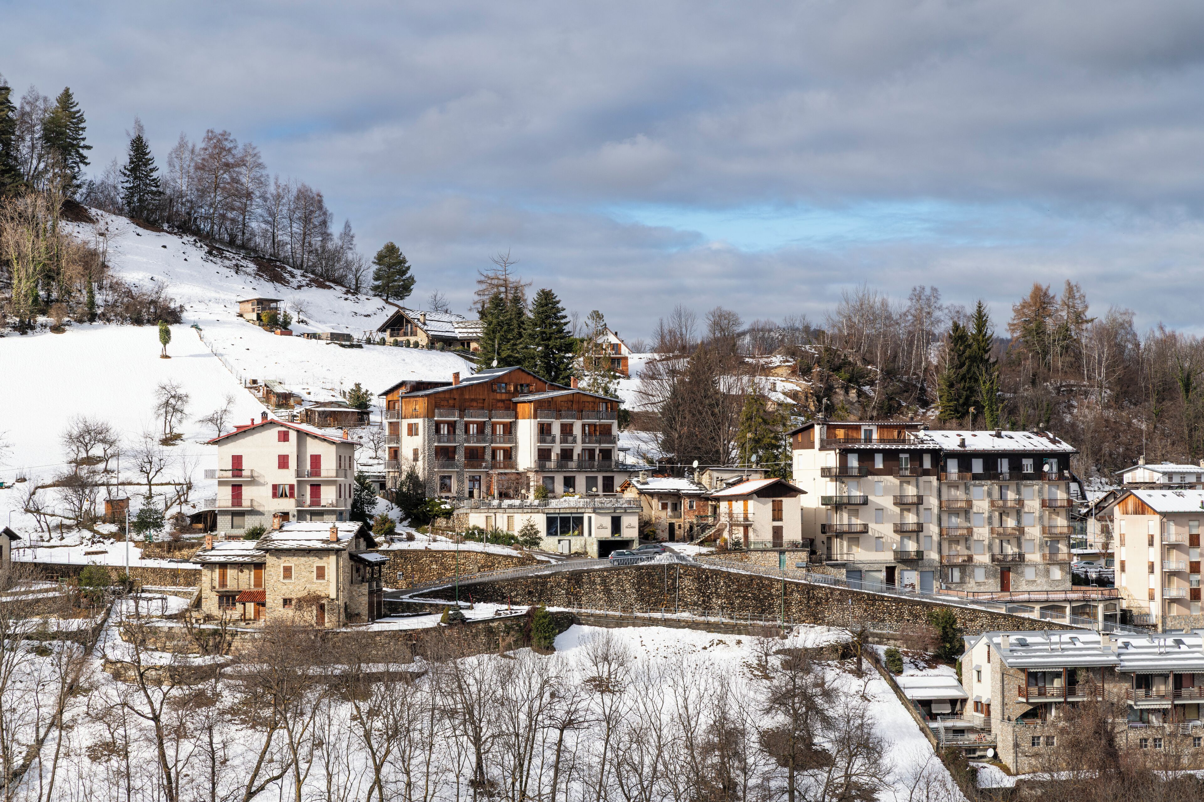 A snow-covered residential area with multi-story buildings, some with balconies, and a hilly backdrop.