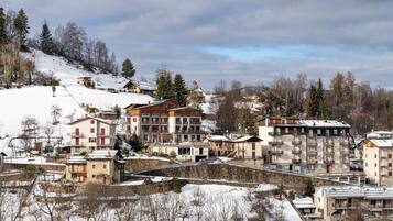 A snow-covered residential area with multi-story buildings, some with balconies, and a hilly backdrop.