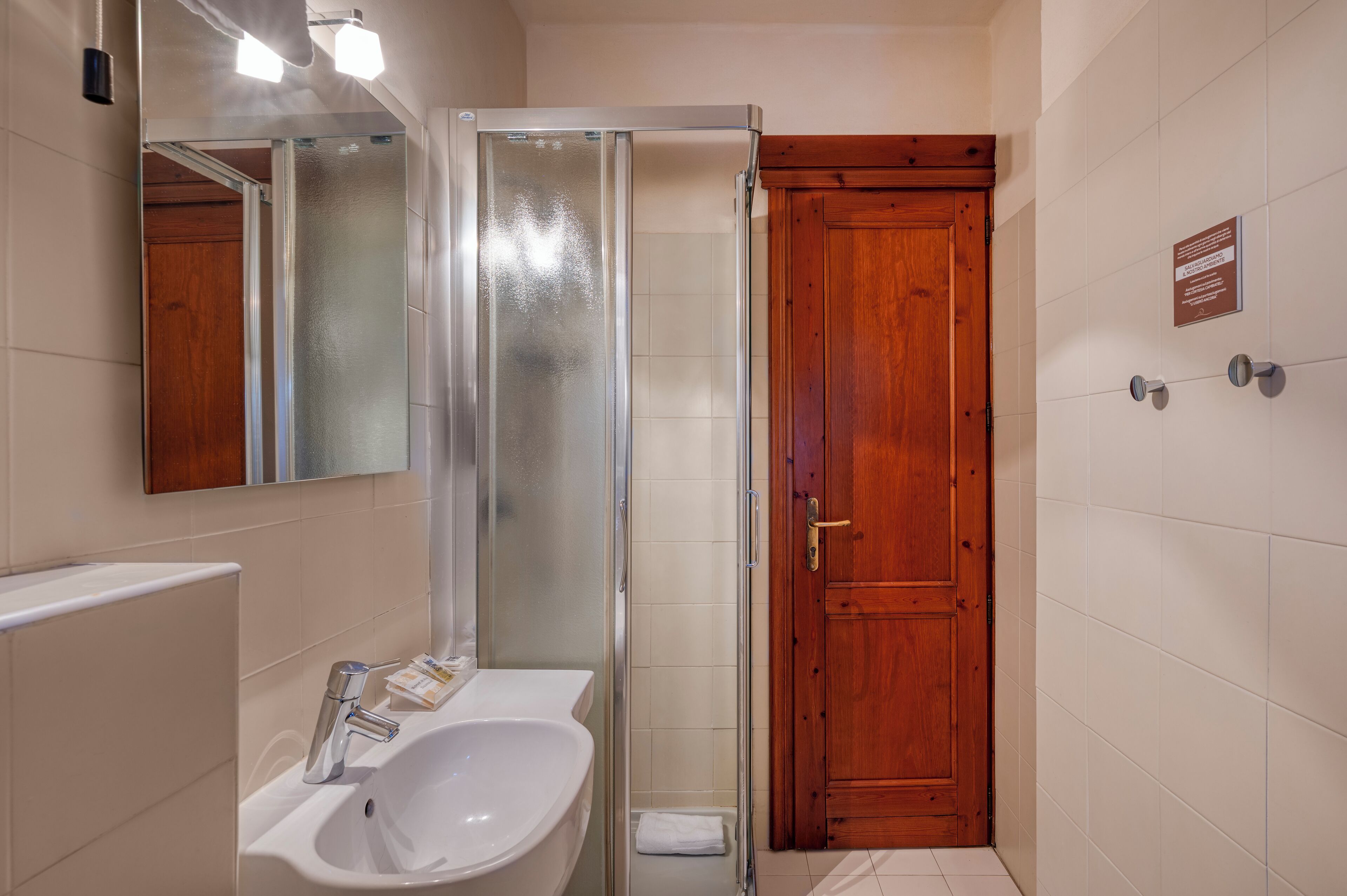 A bathroom with a glass shower enclosure, a wooden door, and a white sink with a mirror above it.