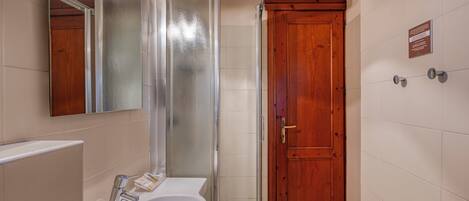 A bathroom with a glass shower enclosure, a wooden door, and a white sink with a mirror above it.