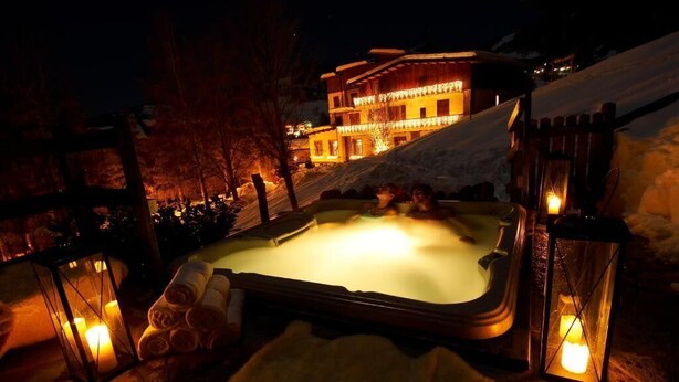 A hot tub surrounded by lanterns, with a snow-covered slope and a building in the background.