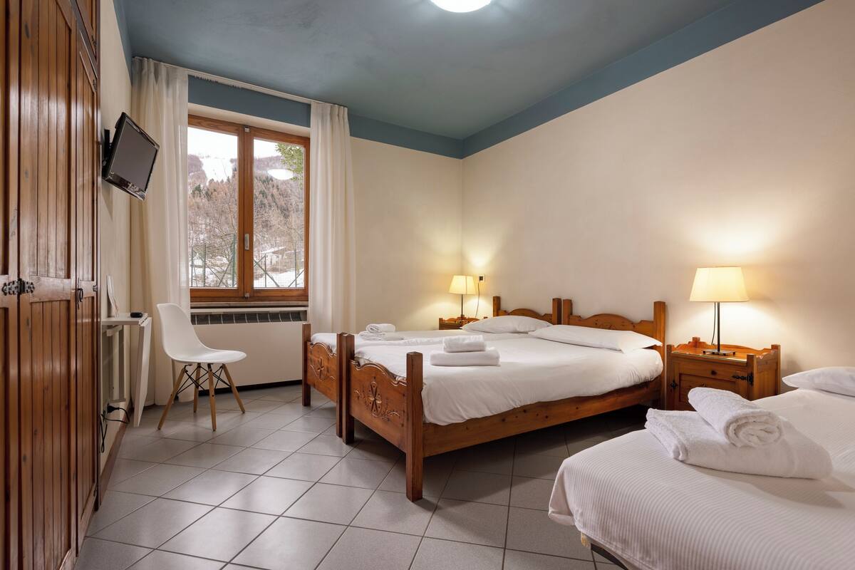 Une chambre d’hôtel avec un lit en bois, un bureau, une chaise et un téléviseur fixé au mur.
