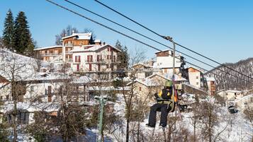 A ski lift with a person in black gear. There are buildings with snow-covered roofs in the background.