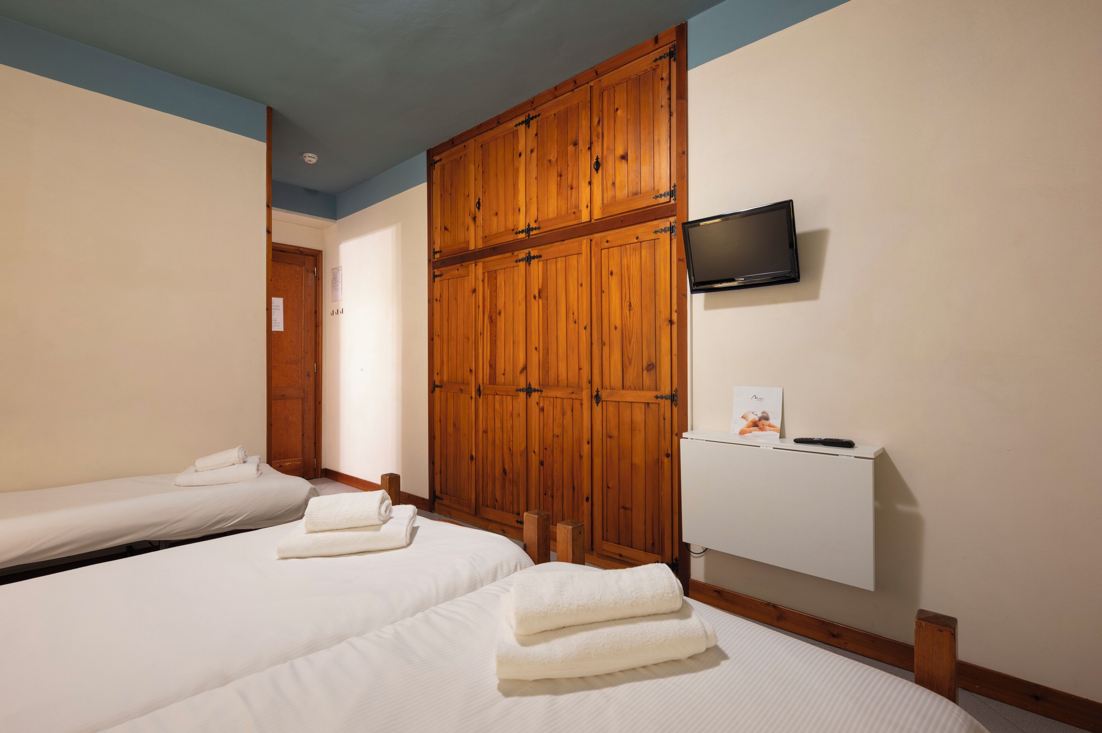 A hotel room with two beds, wooden wardrobe, TV, and a white cabinet.