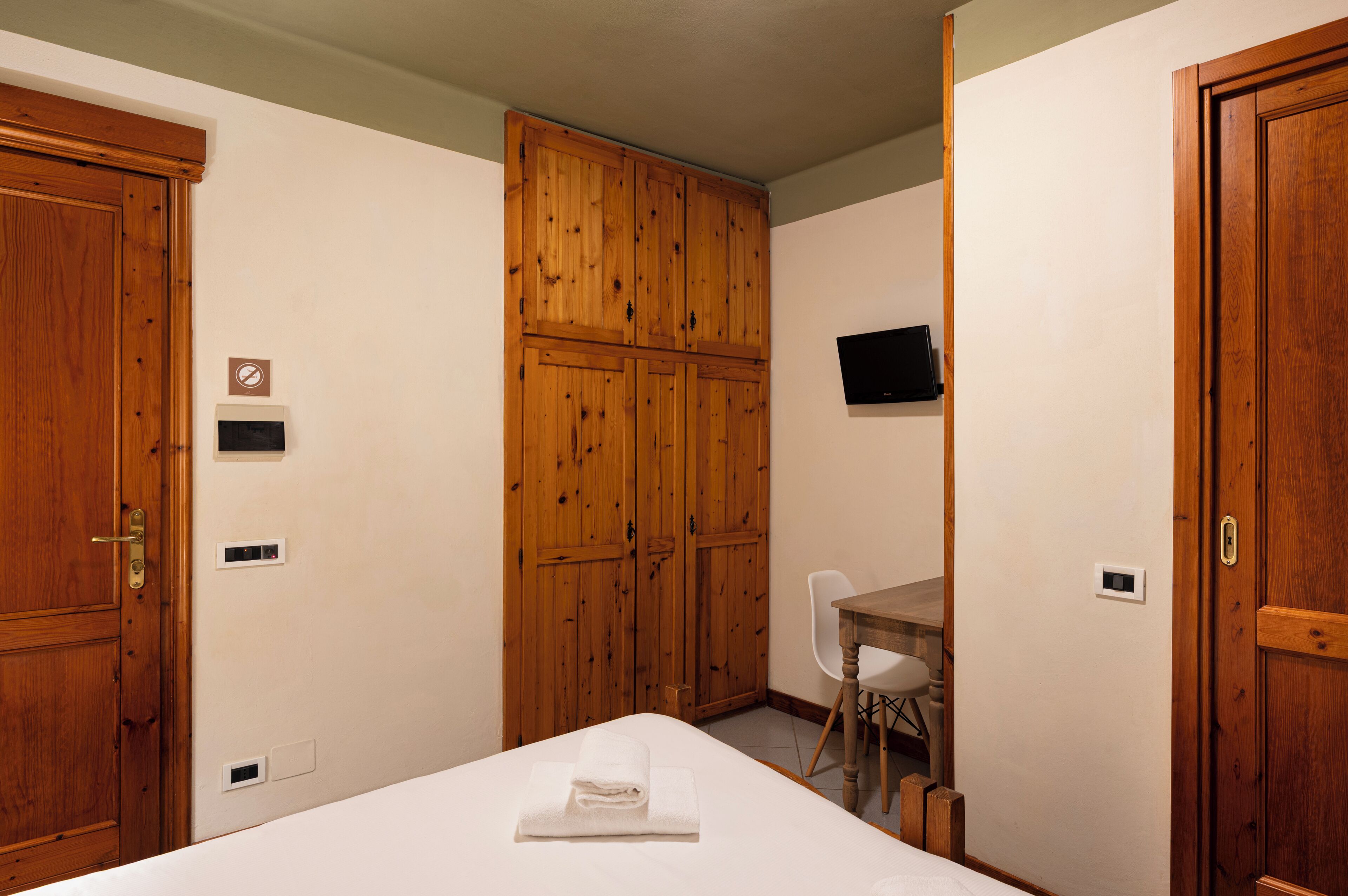 A hotel room with wooden wardrobes, a desk, and a bed with a folded towel.