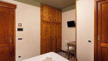 A hotel room with wooden wardrobes, a desk, and a bed with a folded towel.
