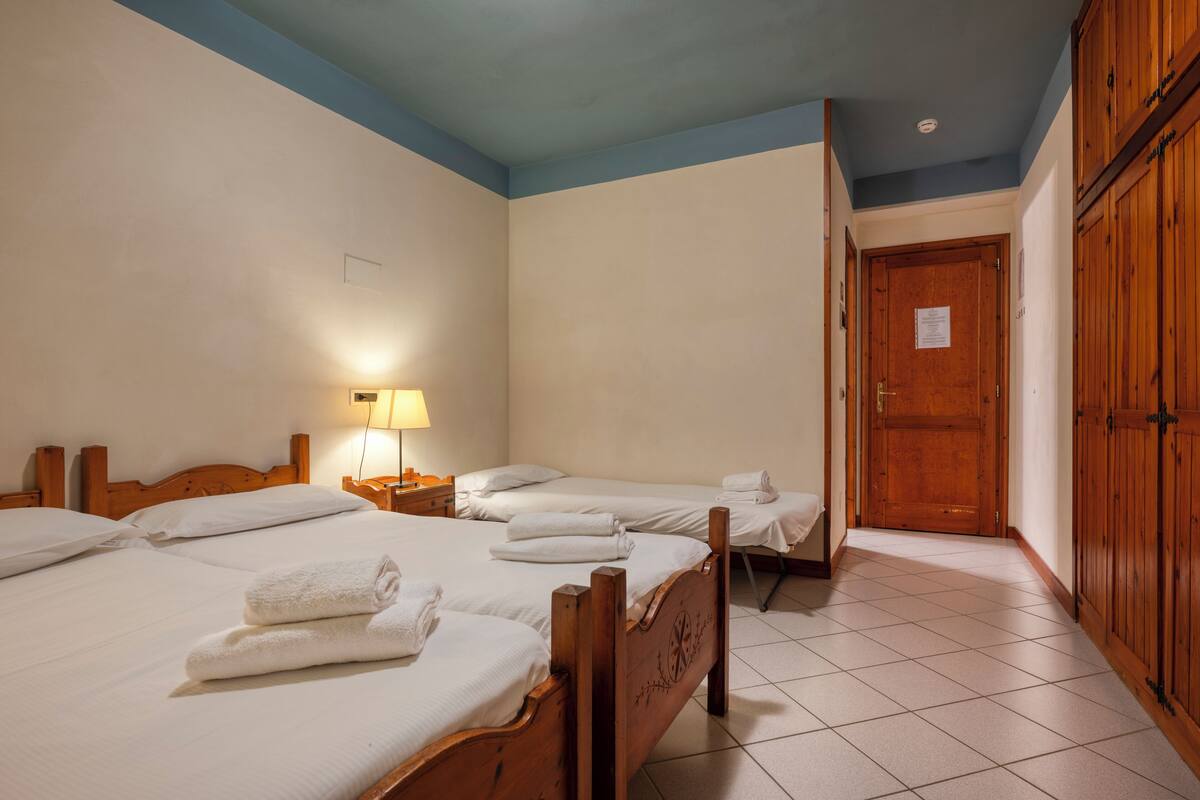 Une chambre d’hôtel avec deux lits, une armoire en bois et un sol carrelé.