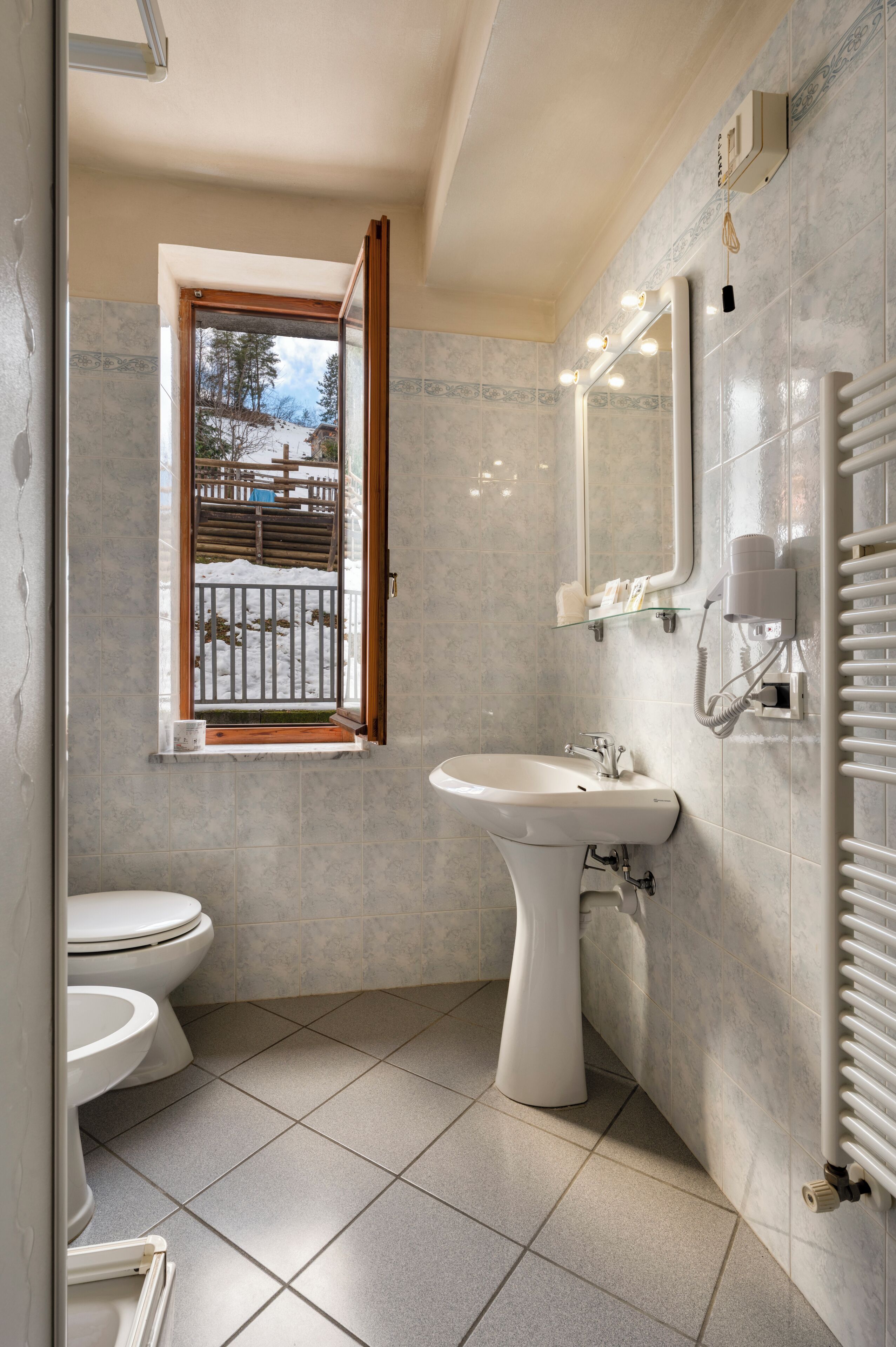 Een badkamer met twee toiletten, een wastafel, een spiegel en een raam met uitzicht op een besneeuwd landschap.